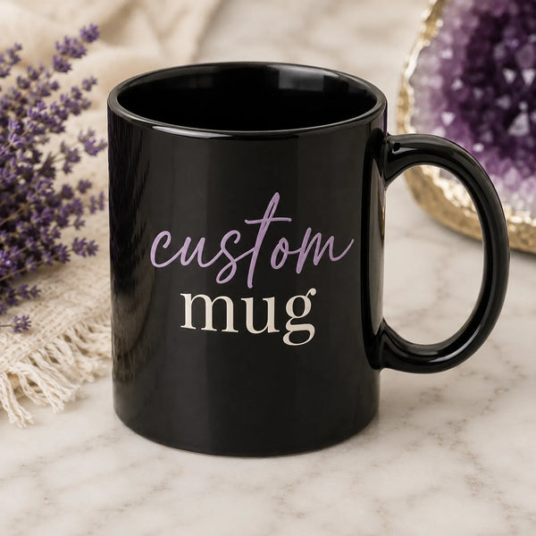 Black ceramic custom coffee mug with 'custom black coffee mug' script and serif text design, styled on marble background with dried flowers and amethyst crystal - Marie Gems