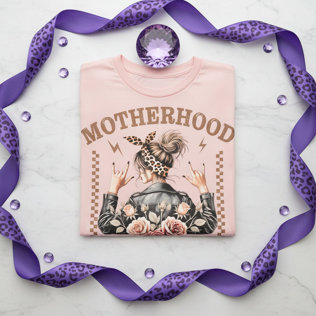 Front design of a light pink motherhood graphic tee featuring floral roses, leopard print accents, and a rocker-inspired mom design displayed in a styled flat lay product photo. 💜