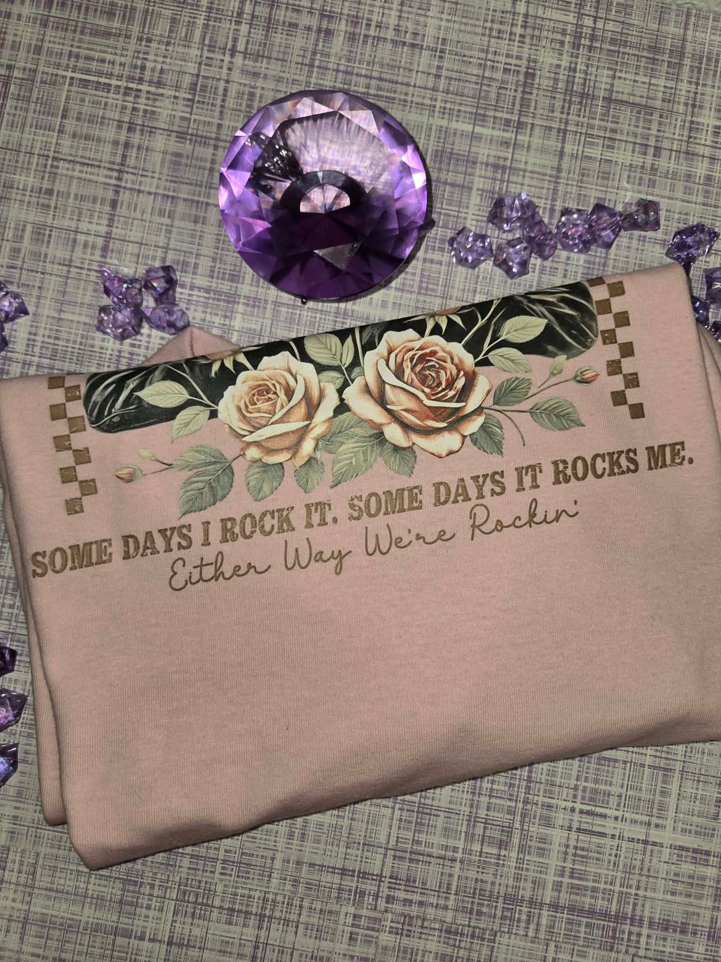 Close-up view of the quote and floral design on a light pink motherhood graphic tee featuring the saying Some Days I Rock It Some Days It Rocks Me Either Way We're Rockin.