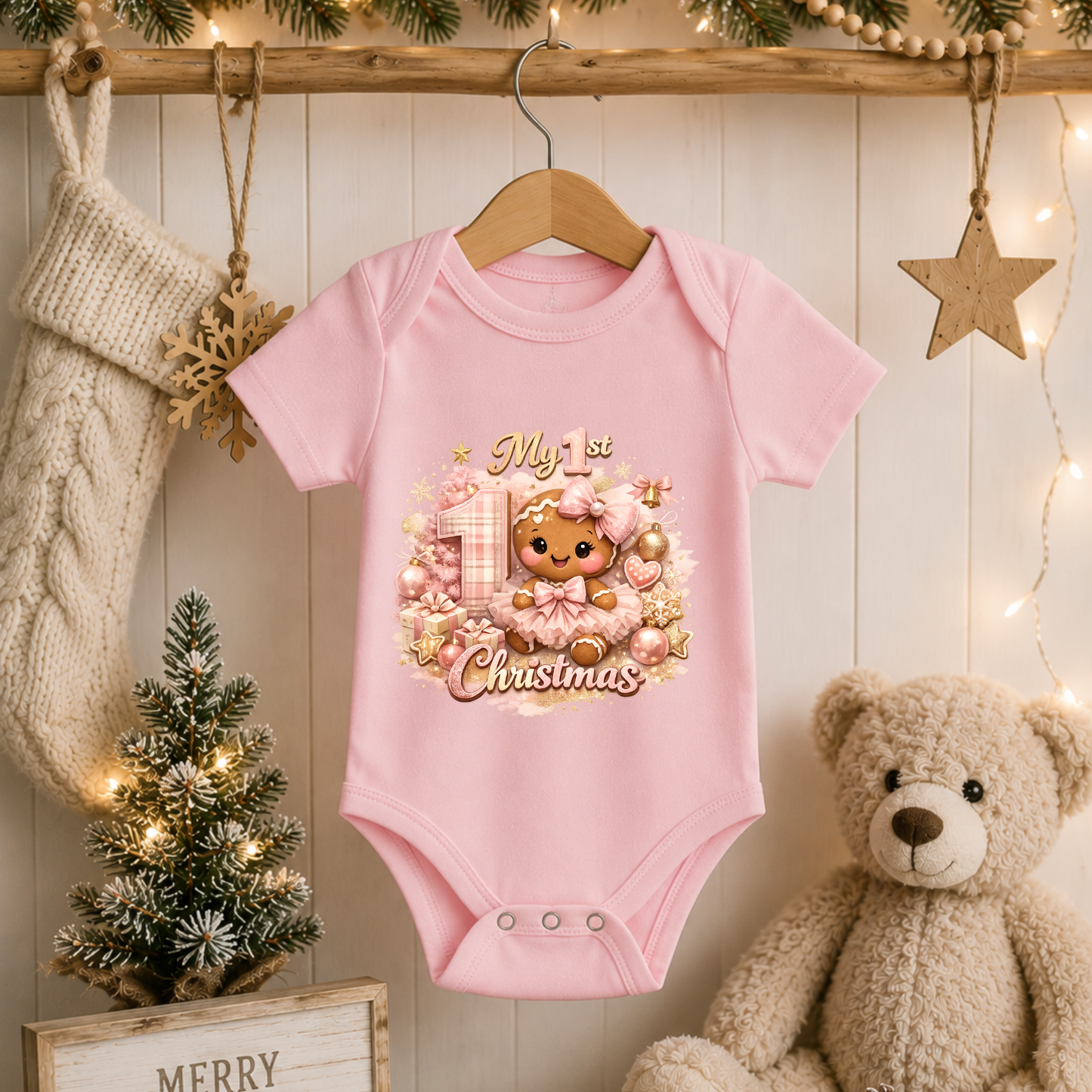 Pink Baby Girl First Christmas bodysuit featuring a festive gingerbread girl design hanging beside a Christmas stocking, miniature tree, and teddy bear.