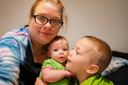 Mom of seven holding her baby while spending time with her toddler during a busy morning of motherhood and running a home business.