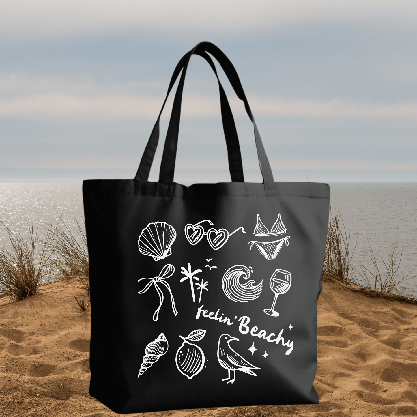 Black Canvas Tote Bag with "Feelin' Beachy" Design featuring white beach-themed icons and text on a reusable 15x16 inch bag.