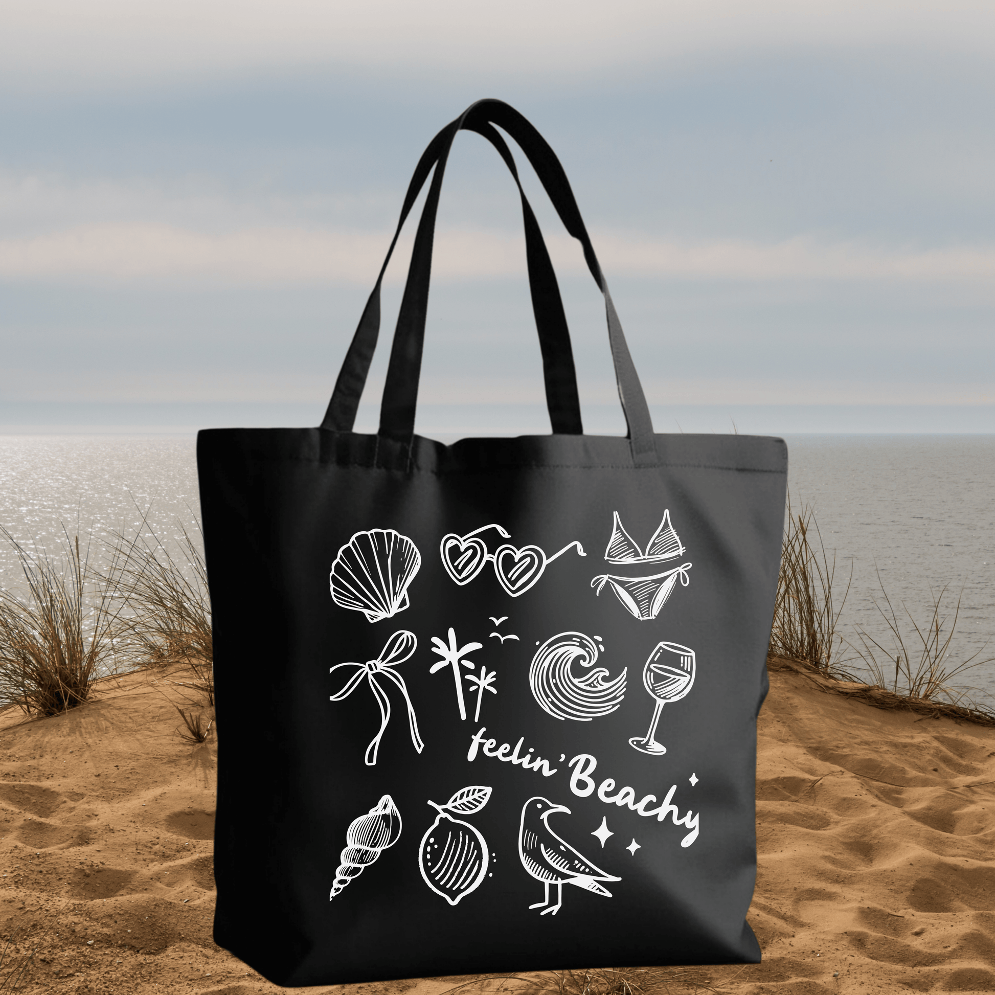 Black Canvas Tote Bag with "Feelin' Beachy" Design featuring white beach-themed icons and text on a reusable 15x16 inch bag.