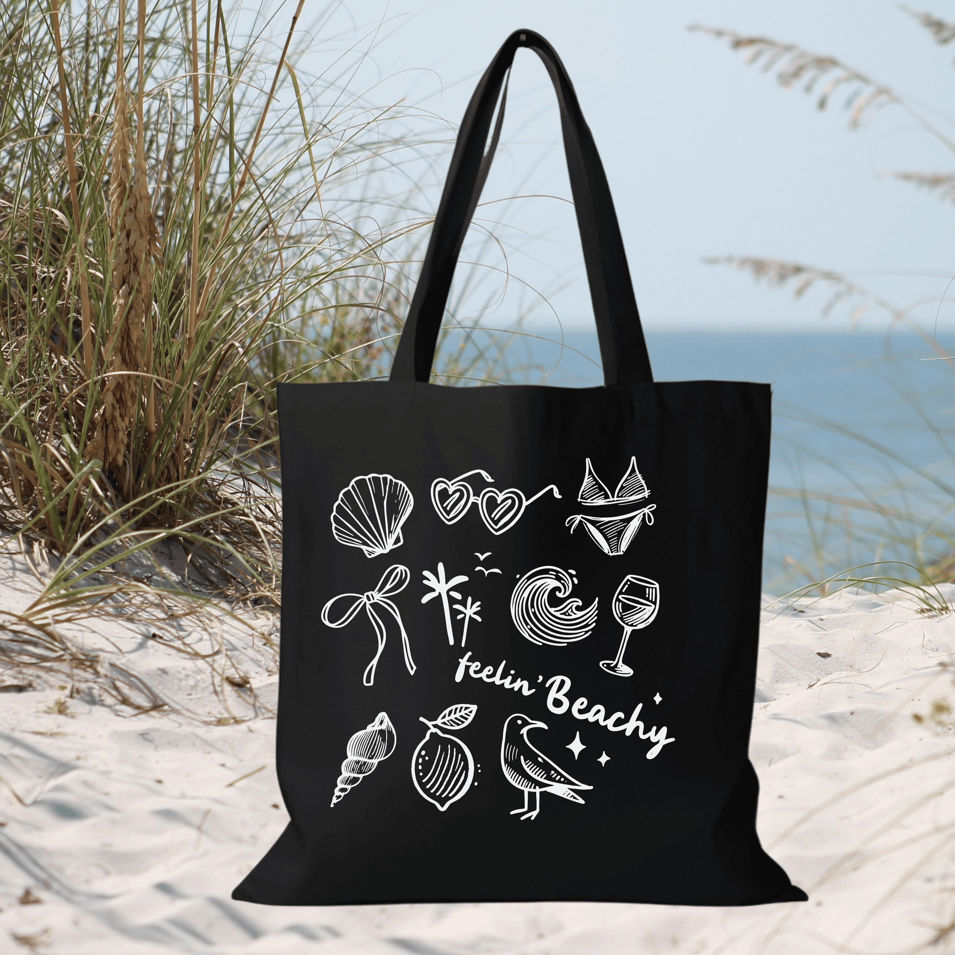 Black Canvas Tote Bag with "Feelin' Beachy" Design featuring white beach illustrations, 15x16 inch reusable shopping bag.