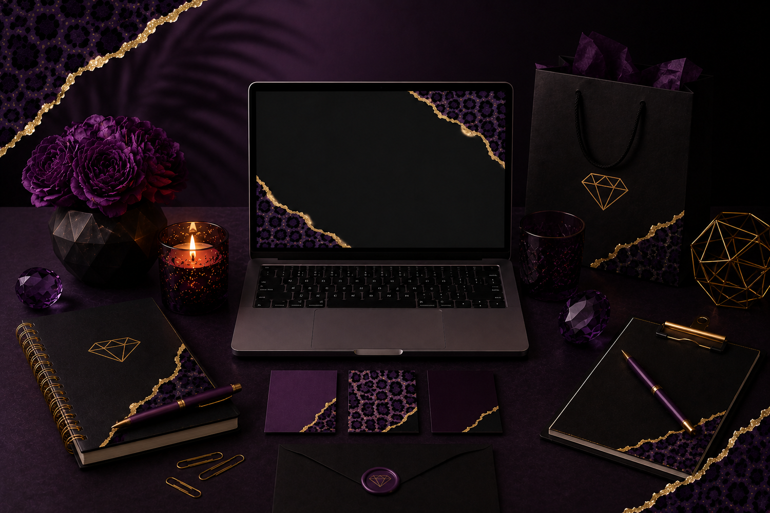 Laptop surrounded by purple and black geometric stationery, floral arrangement, candle, gift bag, and gold accent decor on dark surface