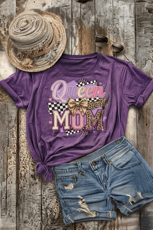 Purple t-shirt with 'Queen Mom' text and denim shorts on a wooden surface