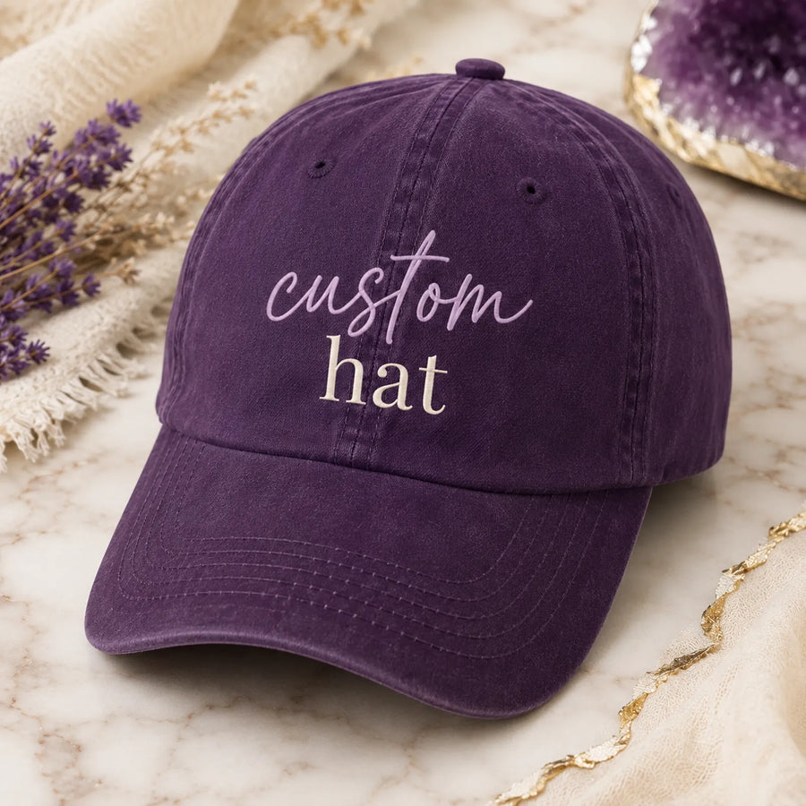 Purple washed cotton dad hat with 'custom hat' script and serif text design, styled on marble background with dried flowers and amethyst crystal - Marie Gems