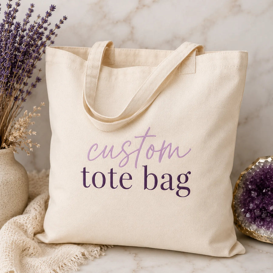 Natural canvas custom tote bag with 'custom tote bag' script and serif text design, styled with dried lavender and amethyst crystal - Marie Gems