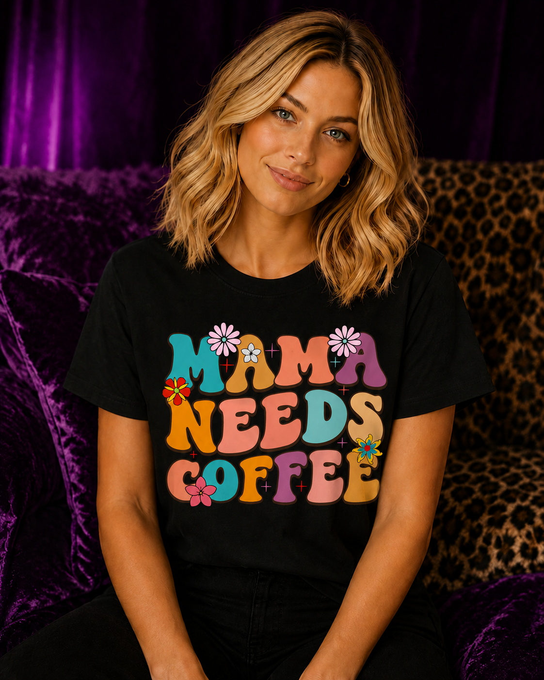 Blonde woman wearing a black Gildan Mama Needs Coffee T-Shirt with colorful retro groovy lettering in a purple velvet and cheetah print setting