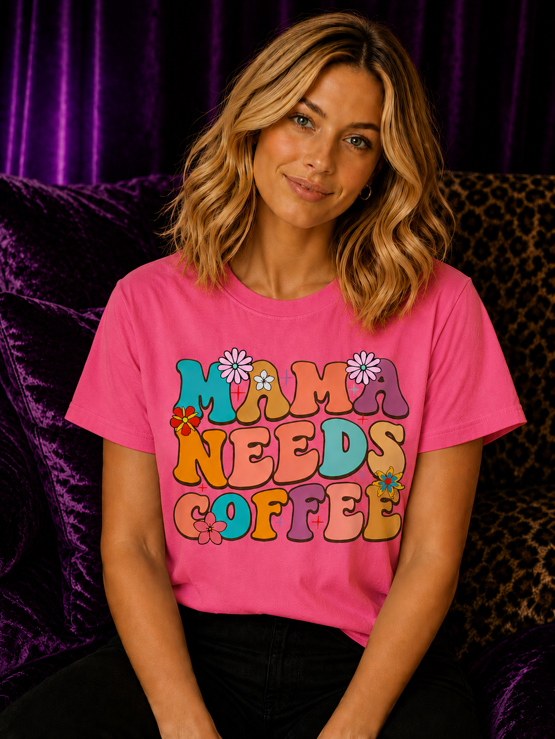 Blonde woman wearing a heliconia pink Gildan Mama Needs Coffee T-Shirt with colorful retro groovy lettering in a cozy aesthetic setting