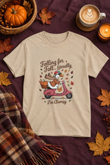 Falling for Fall Literally I'm Clumsy t-shirt in sand with goose on a scooter graphic, styled flat lay with a pumpkin basket, plaid scarf, autumn leaves and a latte