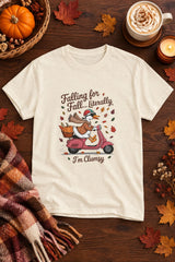 Falling for Fall Literally I'm Clumsy t-shirt in natural with goose on a scooter graphic, styled flat lay with a pumpkin basket, plaid scarf, autumn leaves and a latte