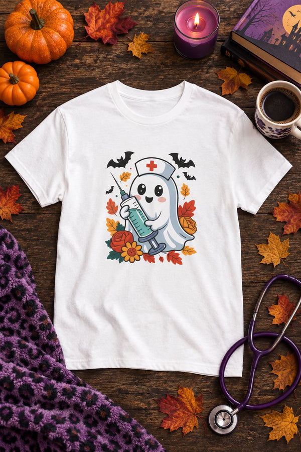 Nurse Ghost Halloween t-shirt in white with cute nurse ghost graphic, styled flat lay with pumpkins, a purple candle, books and a stethoscope