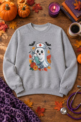 Nurse Ghost Halloween crewneck sweatshirt in sport grey with cute nurse ghost graphic, styled flat lay with pumpkins, a purple candle, books and a stethoscope