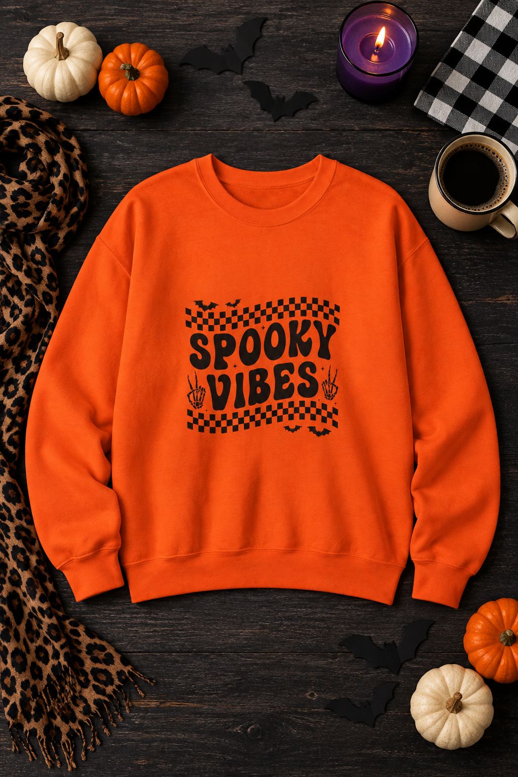Spooky Vibes Retro Checkerboard crewneck sweatshirt in orange with checkerboard Spooky Vibes graphic, styled flat lay with pumpkins, candy corn, bats and a purple candle