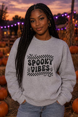 Person wearing the Spooky Vibes Retro Checkerboard crewneck sweatshirt in sport grey with checkerboard Spooky Vibes graphic in a fall setting