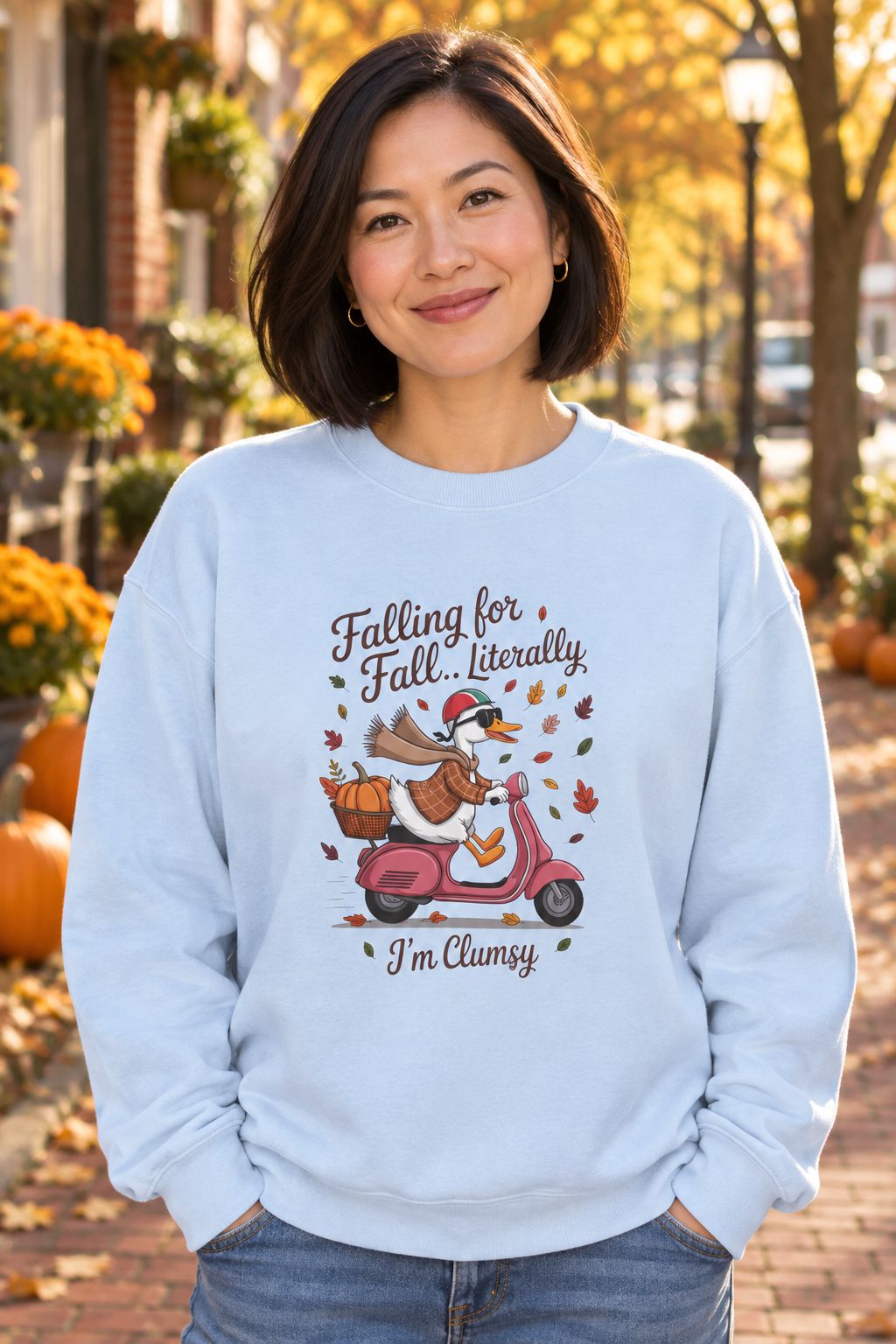 Person wearing the Falling for Fall Literally I'm Clumsy crewneck sweatshirt in light blue with goose on a scooter graphic in a fall setting