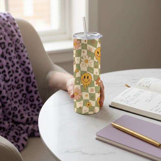 A tall insulated tumbler with a clear lid and straw, featuring a retro checkered pattern with smiley faces, flowers, and stars in muted green, cream, pink, and yellow. The tumbler is centered on a white marble surface with decorative purple glitter corner accents and a purple 'Made just for you' badge in the upper right.