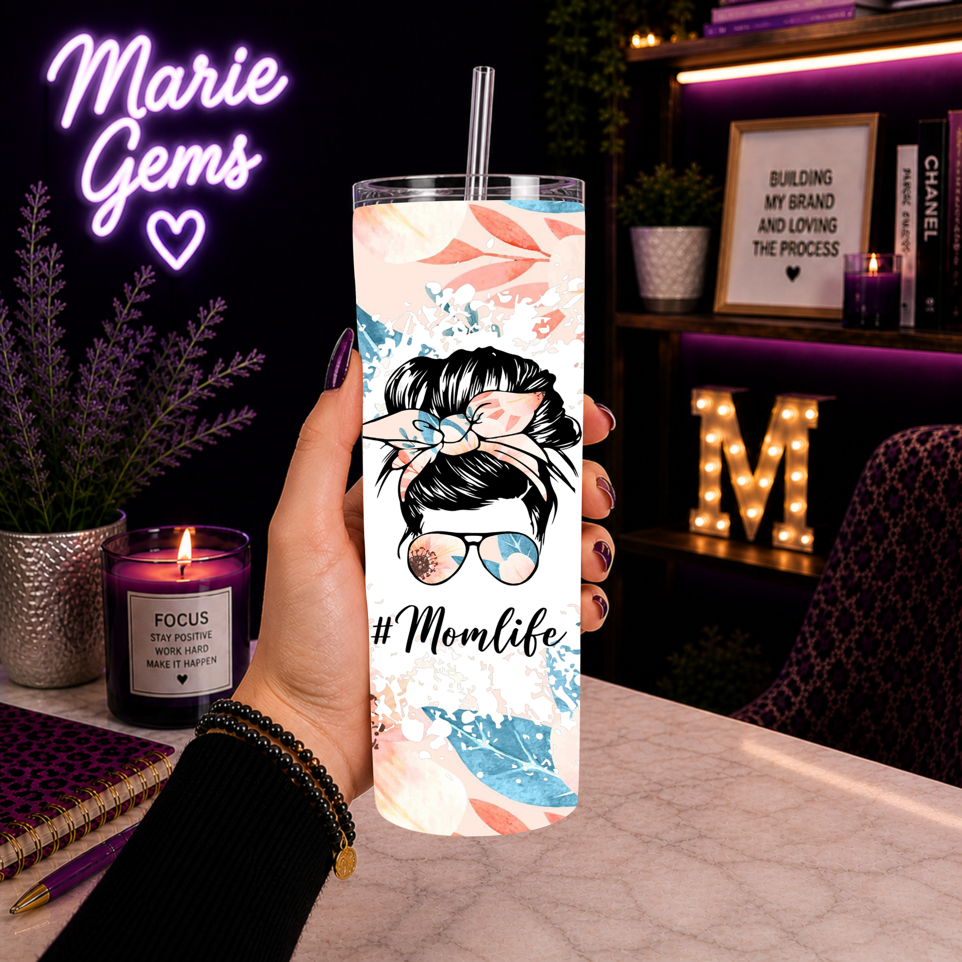 Hand holding Momlife 20oz Tumbler Messy Bun Floral Travel Mug Peach Flower Cup Mothers Day Gift For Her Cute Mama Drinkware in cozy purple-lit room.