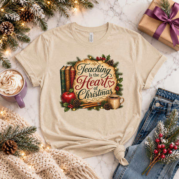 Teaching Is the Heart of Christmas Teacher Unisex Graphic T-Shirt showing Teaching Is the Heart of Christmas with festive books, an apple, greenery, pencils, and a warm drink